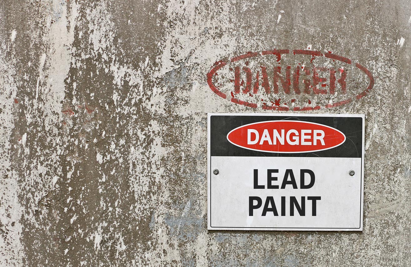 Warning sign for lead paint attached to a weathered wall with significant peeling paint