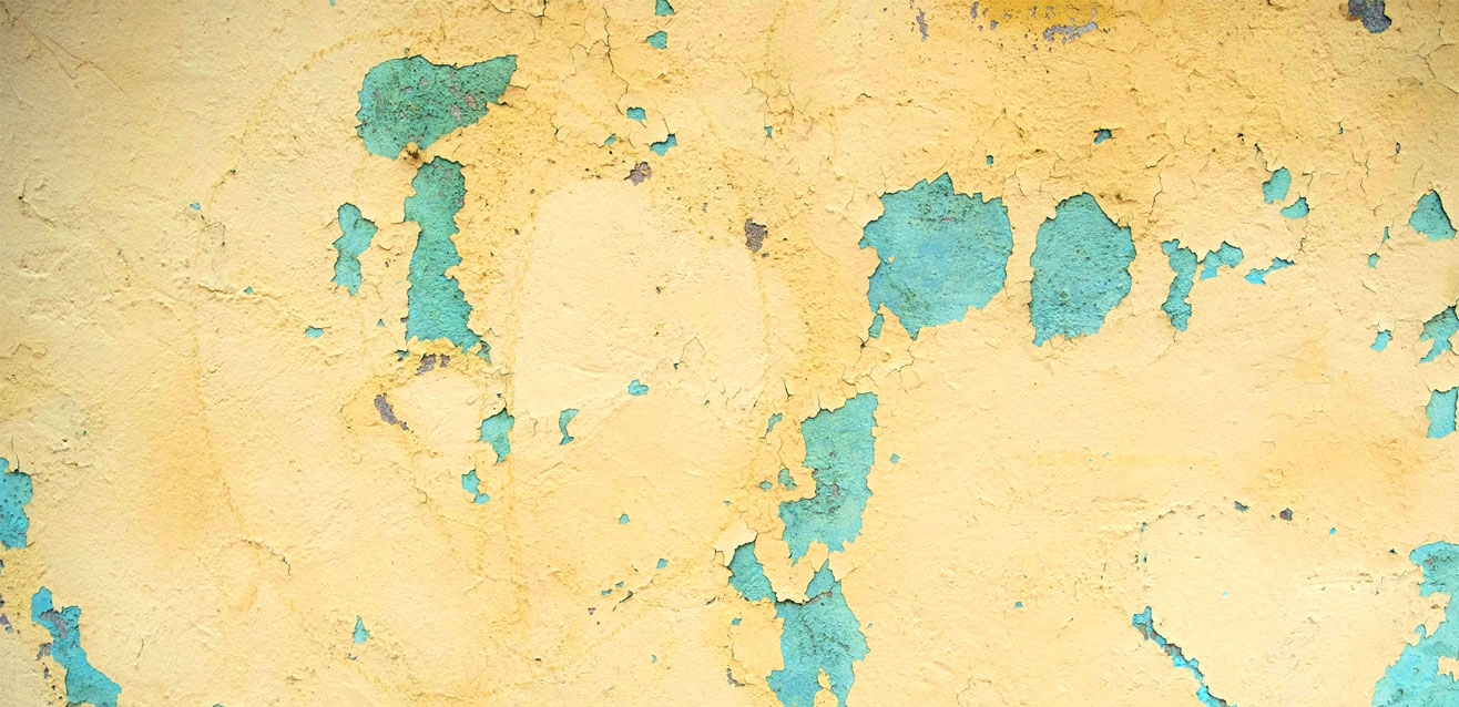 Close-up view of a weathered wall with peeling and crackling paint, revealing layers of texture and color.