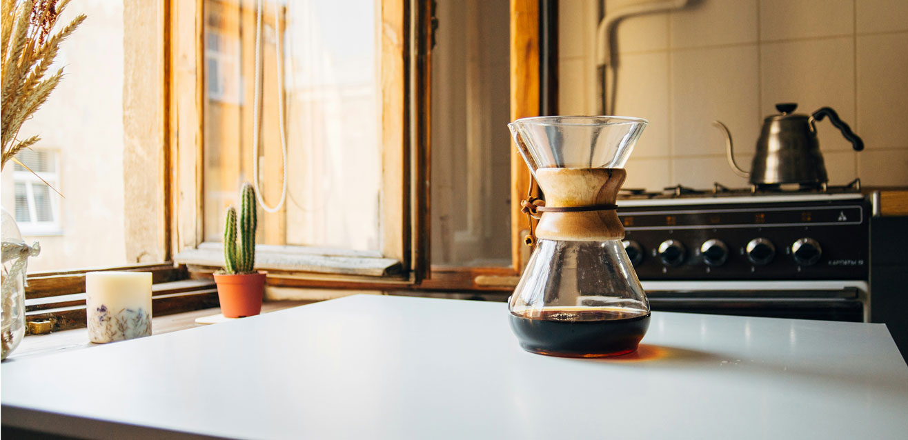 Sunlit kitchen with a coffee maker on the table, a cactus plant by the window, and a stove in the background